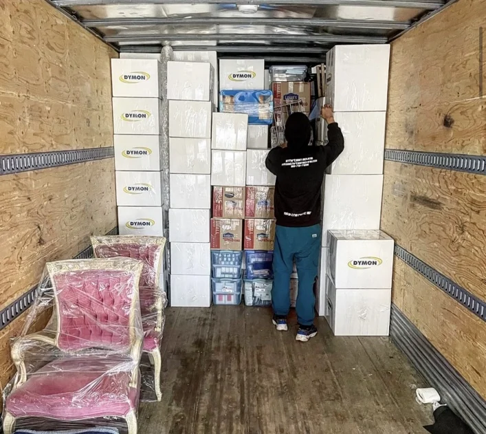 6Thirteen mover loading stacked boxes and wrapped chairs inside a moving truck